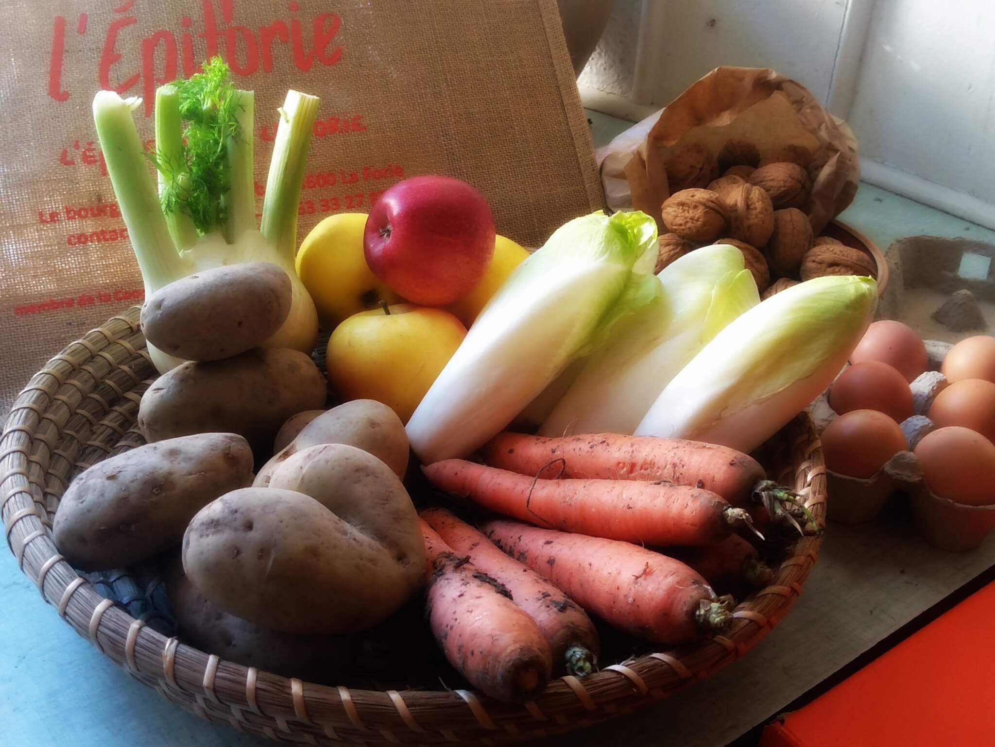 Panier de fruits et légumes avec pommes de terre, carottes, céleri, œufs, pommes et noix.